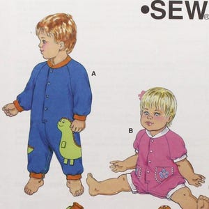 May include: Kwik Sew pattern 3310 for baby sizes S-M-L-XL. The pattern features illustrations of two babies wearing different outfits. One baby is in a blue jumpsuit with a dinosaur applique, and the other is in a pink romper.