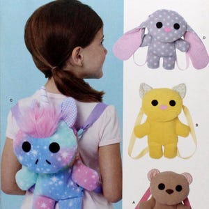 May include: Simplicity sewing pattern S3090 featuring three stuffed animal backpack designs: a bunny, a cat, and a bear. The bunny is gray with pink accents, the cat is yellow, and the bear is brown. The pattern is one size and designed and printed in the USA.