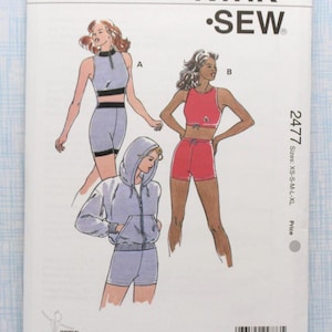 May include: A Kwik Sew sewing pattern, pattern number 2477, featuring illustrations of athletic wear. The pattern includes a zip-up hoodie, shorts, and a crop top. The pattern sizes range from XS to XL.