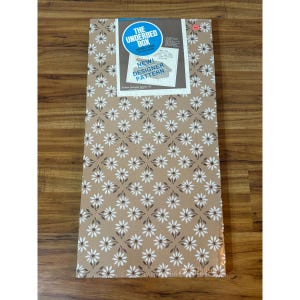 Puede incluir: Una caja rectangular con un estampado floral en blanco y marrón sobre un fondo beige. La caja tiene una etiqueta azul y blanca que dice "THE UNDERBED BOX" y "NEW! DESIGNER PATTERN".