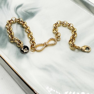 May include: Gold chain bracelet with a small infinity charm set with clear cubic zirconia stones.