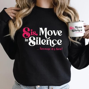 Könnte beinhalten: Schwarzes Sweatshirt mit dem Text "Sis, Move in Silence... because it's time!" in weißer und rosa Schrift. Eine weiße Tasse mit dem gleichen Text wird gehalten.