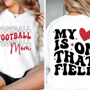 May include: White sweatshirt with the words "FOOTBALL FOOTBALL FOOTBALL Mom" in red and black. The back of the shirt says "MY HEART IS ON THAT FIELD" with a red glitter heart.