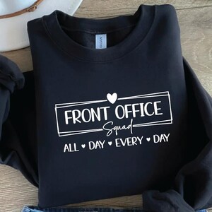 Puede incluir: Sudadera negra con cuello redondo con el texto "FRONT OFFICE Squad" en un rect&aacute;ngulo blanco, con un coraz&oacute;n encima de la palabra "Squad". La frase "ALL DAY EVERY DAY" est&aacute; debajo.