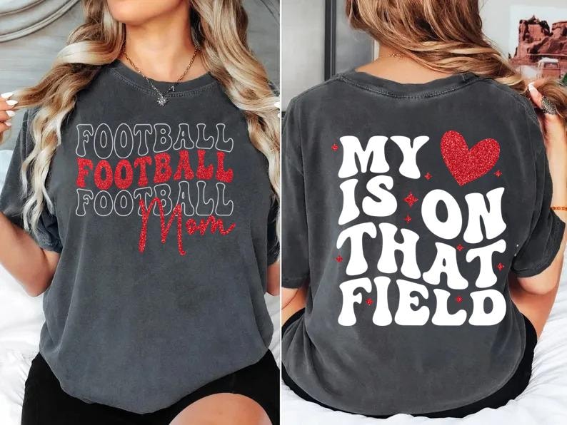 May include: Dark gray t-shirt with the words "FOOTBALL FOOTBALL FOOTBALL Mom" in white and red glitter lettering on the front. The back of the shirt says "MY HEART IS ON THAT FIELD" with a red glitter heart.