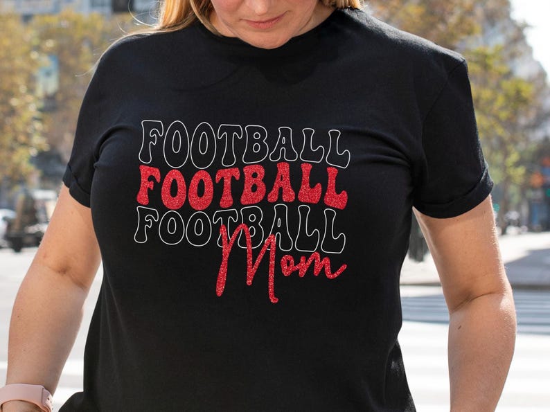 May include: Black t-shirt with the words "FOOTBALL" stacked three times, with the middle one in red glitter and outlined in white. The word "Mom" is written in red glitter below the stacked words.