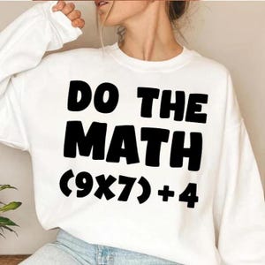 May include: White sweatshirt with the text "DO THE MATH" in bold black letters, followed by the equation (9x7)+4. The sweatshirt has long sleeves and a crew neck.