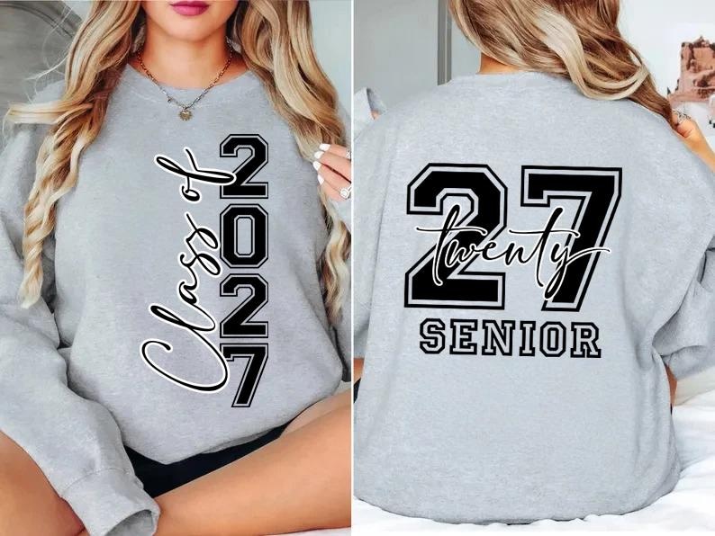 May include: A light gray sweatshirt with the text "Class of 2027" in a vertical script on the front. The back of the sweatshirt features the number "27" with the word "Twenty" and "SENIOR" below it, all in black and white.