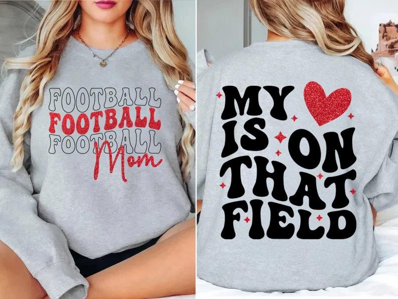 May include: Light gray sweatshirt with the words "FOOTBALL Mom" in red glitter and black lettering on the front. The back of the sweatshirt says "MY IS ON THAT FIELD" with a red glitter heart.