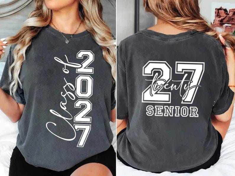 May include: Charcoal gray t-shirt with white text. The front displays "Class of 2027" vertically. The back features "27 Twenty SENIOR" in a bold, collegiate style. A casual, comfortable tee for graduation.