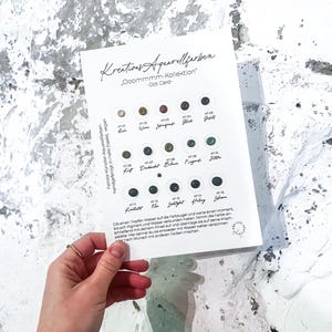 Könnte beinhalten: Eine Hand hält eine weiße Karte mit Aquarellfarben-Mustern. Auf der Karte steht "Kreatives Aquarellfarben" und "Ooommmm-Kollektion - Dot Card." Jede Farbe wird als kleiner Punkt dargestellt.