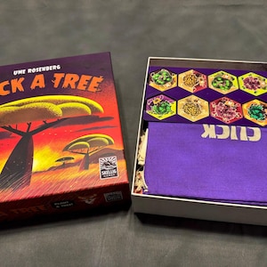 May include: The board game "CLICK A TREE" is shown, with its box and contents. The box has a sunset landscape with acacia trees. Inside, there are hexagonal game pieces and a purple cloth bag with "CLICK" printed on it. The game is by Uwe Rosenberg.
