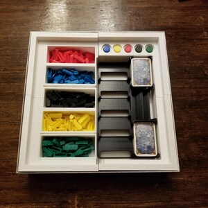 Pu&ograve; includere: Un organizer per giochi bianco con scomparti contenenti pezzi di gioco rossi, blu, neri, gialli e verdi. Ha anche fessure per carte e gettoni colorati. L'organizer &egrave; progettato per mantenere i componenti del gioco ordinati.