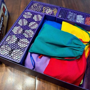 Puede incluir: Una caja de juego de mesa con el título "Steam Power Special Edition" visible. En el interior, un organizador morado contiene piezas de juego, incluyendo fichas y bolsas de colores. Las bolsas son de varios colores: azul, verde, amarillo, rojo y morado.