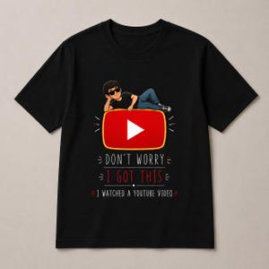 May include: A black short-sleeve t-shirt featuring a graphic of a person wearing sunglasses lying on a red YouTube play button icon. Below the icon, the text reads: DON'T WORRY I GOT THIS I WATCHED A YOUTUBE VIDEO in white and red lettering.