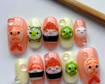 May include: A set of ten artificial nails with a sushi theme. The nails are painted in a light pink and cream color, with various sushi designs, including shrimp, cucumber, salmon, and roe, all with smiling faces.