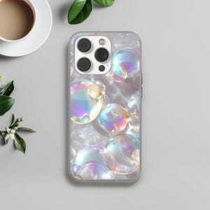 May include: Clear phone case with a pattern of iridescent bubbles. The bubbles have a reflective, rainbow-like sheen, with colors of pink, purple, and yellow. The case has a glossy finish and is designed for a smartphone.