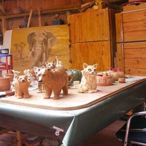 May include: A table with a green tablecloth is covered with ceramic animal figurines, including a bear, a cat, and several birds. There are also several small ceramic pots and a sign that reads "I do yoga".