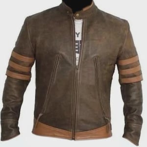 Könnte beinhalten: Eine braune Lederjacke in Distressed-Optik mit Stehkragen und Druckknopfverschluss, durchgehendem Frontreißverschluss sowie drei horizontalen beigen Streifen an jedem Ärmel. Die Jacke besitzt einen beigen Lederbesatz am unteren Saum.