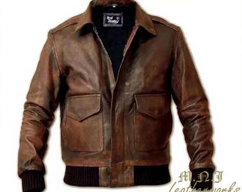 May include: A brown leather jacket with a distressed finish. The jacket features a collared neckline, two front pockets, and a black ribbed hem and cuffs. The interior lining is black. The jacket has the text "Real Leather" and "M.N.J Leatherworks".