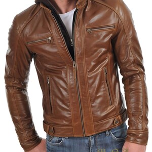 May include: Brown leather jacket with a zip-up front, multiple zippered pockets, and a hooded lining. The jacket has a classic design with a tailored fit. The model is wearing blue jeans. The jacket is from M.N. Leatherworks.