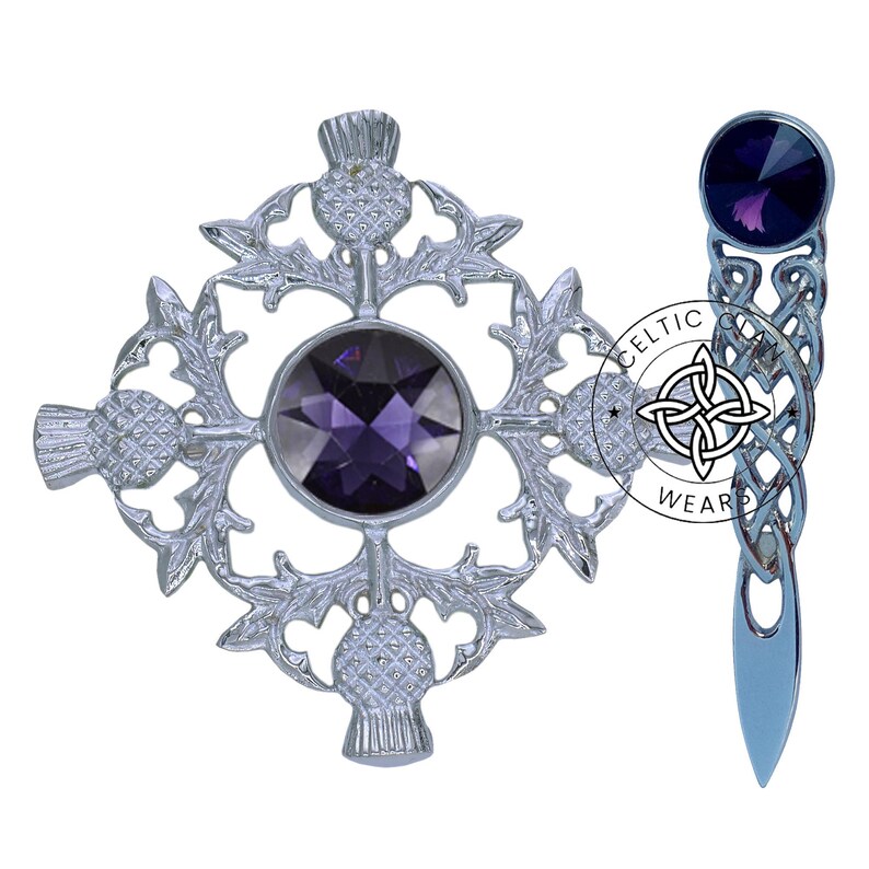 K&ouml;nnte beinhalten: Eine silberne Distelbrosche mit einem violetten Edelstein in der Mitte und eine silberne Kiltnadel mit einem keltischen Knoten und einem violetten Edelstein oben. "Celtic Wear" ist auf der Nadel aufgedruckt.