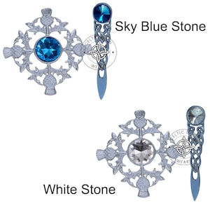 K&ouml;nnte beinhalten: Zwei silberne Kiltnadeln mit einem keltischen Knotendesign und einem Kristallstein in der Mitte. Die obere Nadel hat einen himmelblauen Stein und die untere Nadel einen wei&szlig;en Stein. Der Text "Celtic Wear" befindet sich auf den Nadeln.