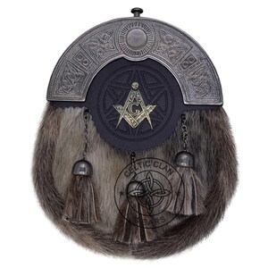 K&ouml;nnte beinhalten: Ein traditioneller schottischer Sporran mit einem Fellk&ouml;rper und einem dekorativen Metallaufsatz. Der Sporran hat eine schwarze Lederklappe mit einem Freimaurersymbol und h&auml;ngenden Quasten. Das Celtic Clan-Logo ist unten sichtbar.
