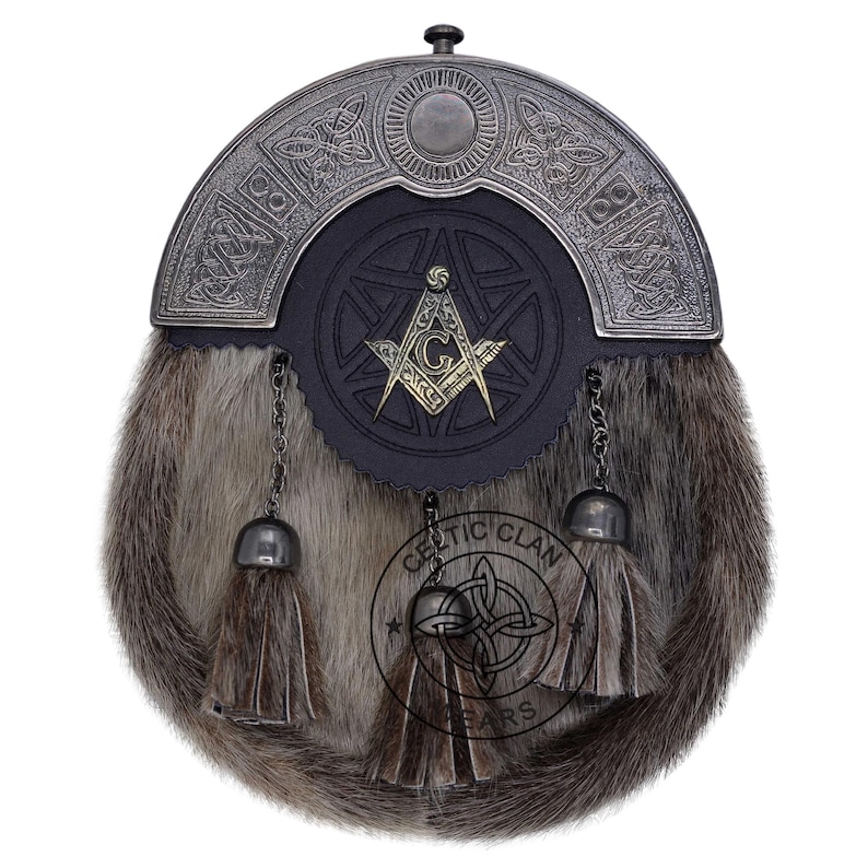 K&ouml;nnte beinhalten: Ein traditioneller schottischer Sporran mit einem Fellk&ouml;rper und einem dekorativen Metallaufsatz. Der Sporran hat eine schwarze Lederklappe mit einem Freimaurersymbol und h&auml;ngenden Quasten. Das Celtic Clan-Logo ist unten sichtbar.