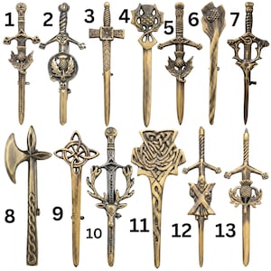 May include: A collection of thirteen metallic kilt pins and brooches in antique gold and silver tones. The designs include various sword, axe, and thistle motifs, along with intricate Celtic knotwork and animal imagery, each numbered one through thirteen.