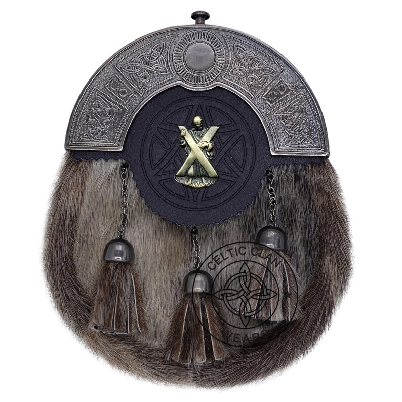 K&ouml;nnte beinhalten: Ein traditioneller schottischer Sporran mit einem Fellk&ouml;rper und einem dekorativen Metallaufsatz. Der Sporran hat eine schwarze Lederklappe mit einem Metallabzeichen und drei h&auml;ngenden Quasten. Das Celtic Clan-Logo ist sichtbar.