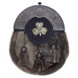 K&ouml;nnte beinhalten: Ein traditioneller schottischer Sporran mit einem Fellk&ouml;rper und einem dekorativen Metall-Cantle. Der Sporran hat eine schwarze Lederfront mit einem goldenen Kleeblatt-Emblem und h&auml;ngenden Quasten. Der Cantle hat keltische Knotenmuster.