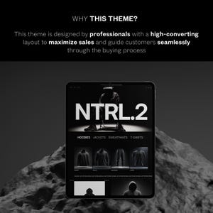 May include: A digital tablet shows a website with the text "NTRL.2" in bold white letters. The website displays clothing items such as hoodies, jackets, sweatpants, and t-shirts. The image is in grayscale, with a dark background and a rocky foreground.