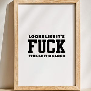 May include: A framed print with the text "LOOKS LIKE IT'S FUCK THIS SHIT O'CLOCK" in bold black letters on a white background. The frame is made of light-colored wood.