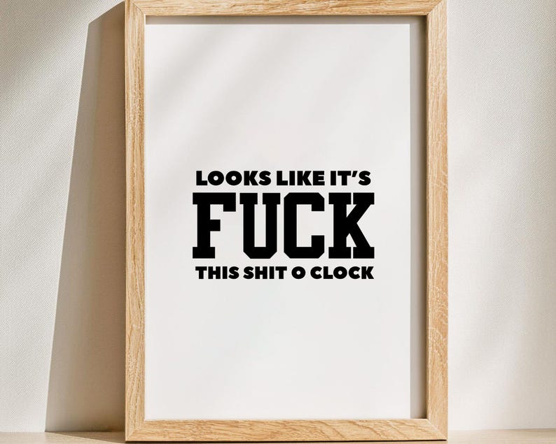 May include: A framed print with the text "LOOKS LIKE IT'S FUCK THIS SHIT O'CLOCK" in bold black letters on a white background. The frame is made of light-colored wood.