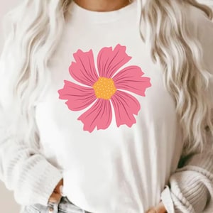 May include: White long-sleeved shirt featuring a large pink flower with a yellow center. The flower design is centered on the shirt's front. The shirt has a crew neck and is made of a soft, comfortable material.