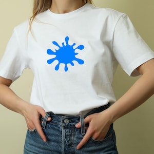 May include: White t-shirt with a large blue paint splatter design. The short-sleeved shirt is made of a soft material and is worn with blue denim jeans. The casual top is suitable for everyday wear.