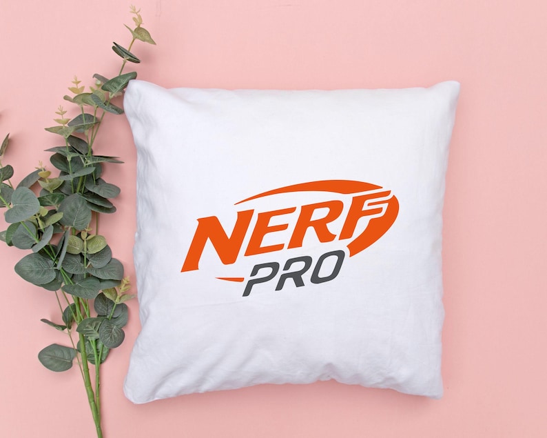 May include: White square pillow with the orange and gray "NERF PRO" logo. The pillow is on a pink background with green and gray leaves.