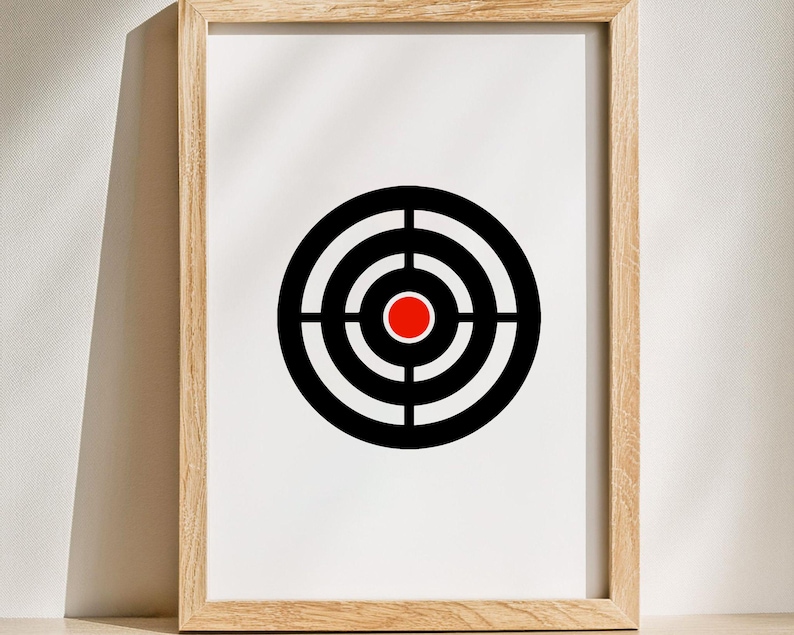 May include: Framed print featuring a target design. The target has concentric black and white rings with a red center. The print is set in a light brown wooden frame, creating a minimalist aesthetic.