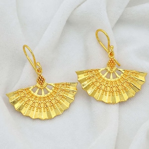 Może przedstawiać: Para złotych kolczyków w kształcie wachlarza. Kolczyki są delikatne i misterne, z fakturowaną powierzchnią.