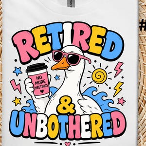 May include: White t-shirt featuring a cartoon goose wearing sunglasses and holding a coffee cup. The shirt has the words "RETIRED & UNBOTHERED" in colorful bubble letters, along with graphics of a sun, lightning bolts, and stars.