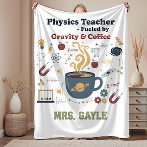 Könnte beinhalten: Weiße Fleece-Decke mit dem Text "Physics Teacher - Fueled by Gravity & Coffee" und dem Namen "MRS. GAYLE". Das Design umfasst wissenschaftliche Illustrationen, eine Kaffeetasse mit einem Planeten und physikalische Gleichungen.