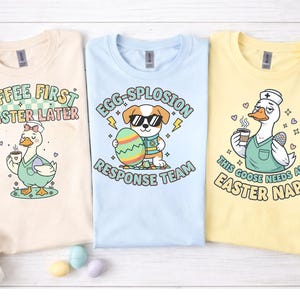 May include: Three pastel-colored t-shirts with Easter-themed graphics. One shirt is cream-colored with a duck holding coffee and the text "COFFEE FIRST EASTER LATER". Another is light blue with a dog holding an egg and the text "EGG-SPLOSION RESPONSE TEAM". The last is yellow with a goose and the text "THIS GOOSE NEEDS AN EASTER NAP".