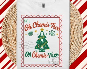 Pode incluir: Camiseta branca com um gráfico temático de Natal. O design apresenta uma árvore de Natal verde feita de equipamentos de laboratório, com as palavras "Oh Chemis-Tree" em vermelho e verde, e uma borda de selo postal.