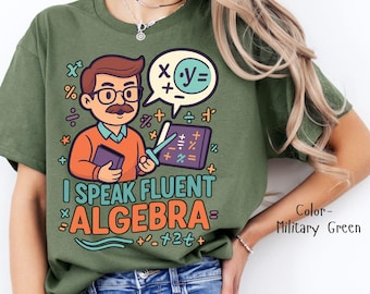 Può includere: T-shirt verde oliva con una grafica raffigurante un insegnante di cartoni animati che tiene in mano un libro e un puntatore. Il testo "I Speak Fluent Algebra" è in un design colorato, con simboli matematici. Il colore della maglietta è "Military Green".