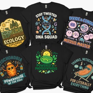 May include: Several black t-shirts with science-related designs. The shirts display phrases such as "Ecology Explorer," a DNA strand with "DNA Squad," and illustrations about cell division and photosynthesis. Other shirts feature mitochondria with text like "Powerhouse of the Cell."