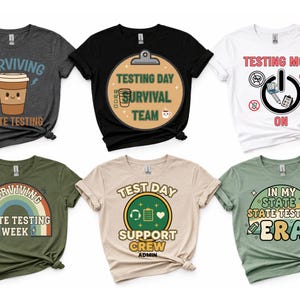 May include: Six t-shirts with various designs related to state testing. The shirts are in different colors, including gray, black, white, olive green, and tan. Each shirt features a unique graphic and text, such as "Surviving State Testing" and "Testing Mode On."