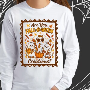 Può includere: Maglietta bianca a maniche lunghe con una grafica incorniciata marrone. La grafica mostra il testo "Are You FALL-O-WEEN Creations?" e presenta tre fantasmi dei cartoni animati, una zucca e foglie d'autunno.