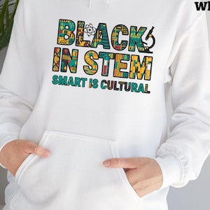 Könnte beinhalten: Weißer Kapuzenpullover mit Fronttasche und dem Text "BLACK IN STEM SMART IS CULTURAL" in bunten Blockbuchstaben. Das Design enthält wissenschaftsbezogene Symbole und Muster.