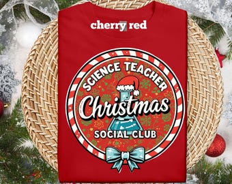 Pode incluir: Camiseta vermelho cereja com um gráfico circular. O gráfico diz "Science Teacher Christmas Social Club" com um béquer usando um chapéu de Papai Noel e um laço azul. A camisa é dobrada em uma superfície tecida.